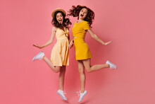 Girl In Mini Dresses Jump On Pink Background. Beautiful Ladies With Dark Hair In White Modern Sneakers Posing For Camera