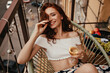 © Look! - Pretty lady looks into camera, holds white wine glass and sits on terrace. Young stylish girl in good mood relaxing on terrace with champagne