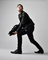full length portrait of a brunette man wearing leather jacket and holding a science fiction gun. sta