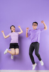 Wall Mural - Young Asian couple jumping on purple background