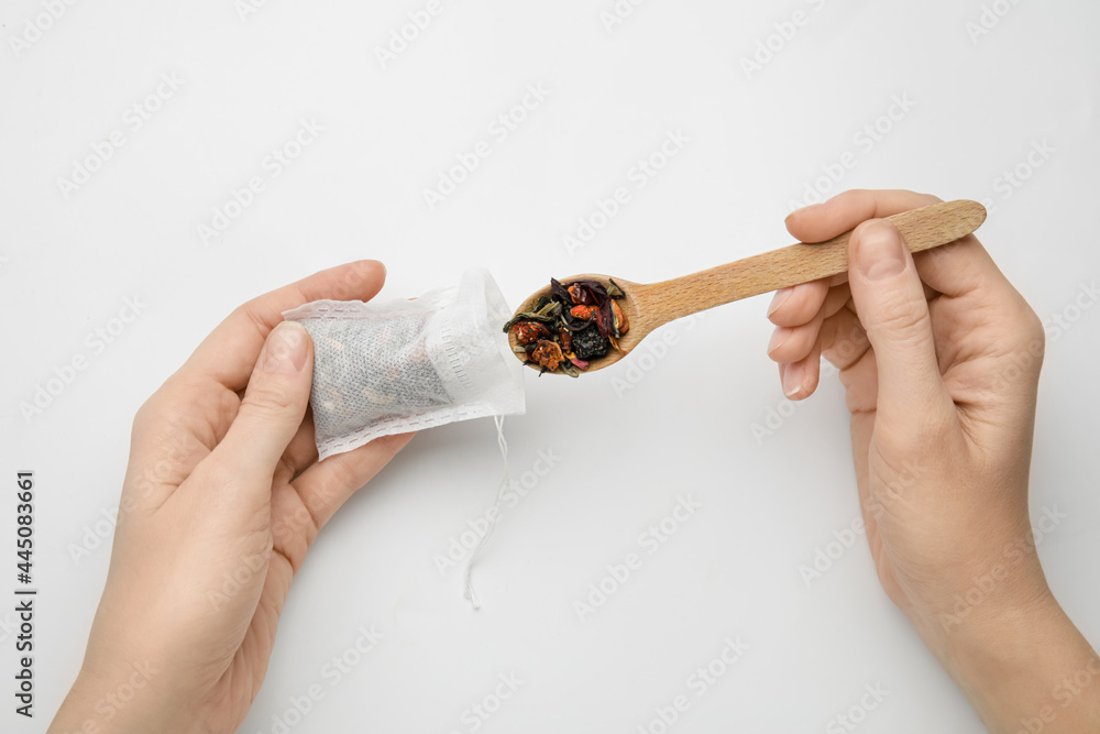 Woman putting dry tea leaves in bag on white background