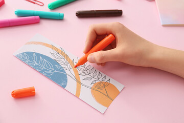 Wall Mural - Woman coloring bookmark on color background, closeup