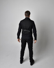 Wall Mural - Full length portrait of a brunette man wearing black shirt and gothic waistcoat.  Standing pose isolated  against a grey studio background.