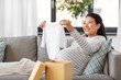 © Syda Productions - pregnancy, holidays and people concept - happy smiling pregnant asian woman opening gift box with baby's bodysuit at home