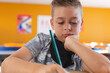 © WavebreakMediaMicro - Caucasian schoolboy with face mask sitting in classroom concentrating and writing in schoolbook