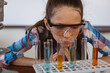 © WavebreakMediaMicro - Caucasian schoolgirl wearing safety glasses looking at test tubes in science class
