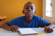 © WavebreakMediaMicro - Portrait of african american schoolboy sitting at desk with notebook in classroom