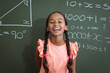 © WavebreakMediaMicro - Portrait of laughing mixed race schoolgirl standing in front of chalkboard in classroom maths lesson