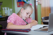 Caucasian schoolgirl at desk in classroom writing and using laptop