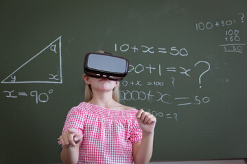 Wall Mural - Caucasian schoolgirl standing at chalkboard in classroom wearing vr headset