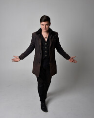 Wall Mural - Full length portrait of a brunette man wearing black leather coat.  Standing pose isolated against a grey studio background.