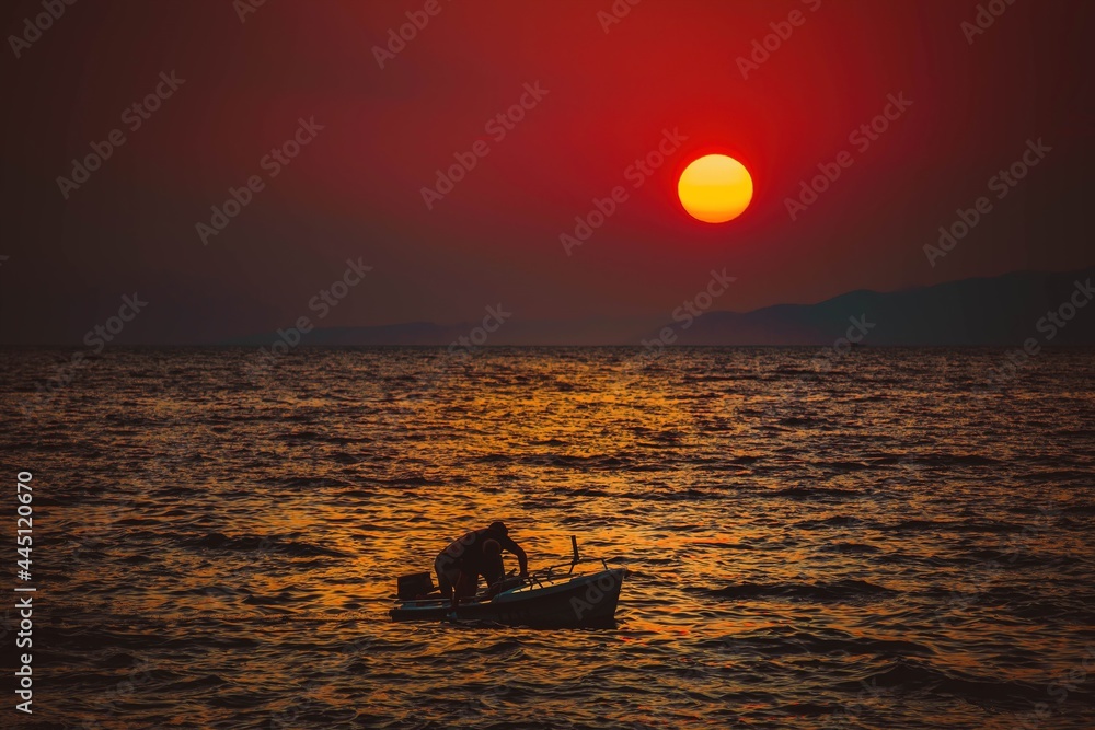 Pływający ludzie na morzu na tle ogromnego zachodzącego słońca - obrazy, fototapety, plakaty 