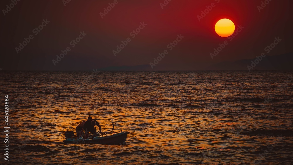Pływający ludzie na morzu na tle ogromnego zachodzącego słońca - obrazy, fototapety, plakaty 