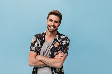 Wall Mural - Wonderful young man with red beard in printed black shirt and grey cool t-shirt looking into camera, crossing his arms and smiling..