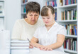 Old teacher helps to girl with syndrome doing homework at library. Education for disabled children concept