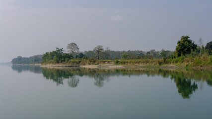 Wall Mural - Peaceful landscape panorama of Brahmaputra river bank with trees reflection in water in remote rural Assam, India