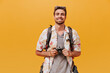 Smiling tourist with ginger beard in short sleeve summer shirt and plaid t-shirt holding camera and smiling on orange backdrop..