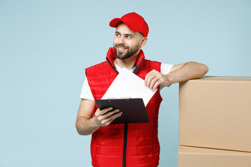 Wall Mural - Professional delivery guy employee man in red cap white T-shirt vest uniform workwear work as dealer courier hold blank cardboard box isolated on pastel blue color background studio. Service concept.