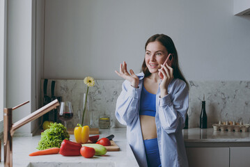 Wall Mural - Young excited fun housewife happy woman 20s in casual clothes blue shirt prepare salad talk by mobile cell phone look overhead cook food in light kitchen at home alone Healthy diet lifestyle concept.