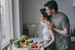 © ViDi Studio - Young side view happy couple two married woman man in casual t-shirt clothes look at window far away distance hug wife cooking food in light kitchen at home together Healthy diet lifestyle concept.