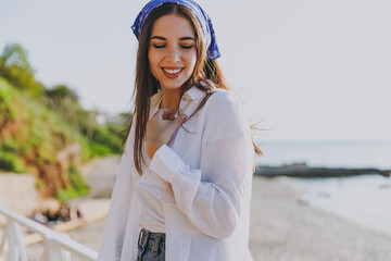 Beautiful young satisfied happy traveler tourist woman in blue bandana white shirt summer casual clothes standing resting outdoors at sea beach background People vacation lifestyle journey concept