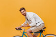 © Look! - Positive bearded man with brown hair in stylish jacket and beige cool shorts smiling and sitting on bicycle on isolated backdrop..