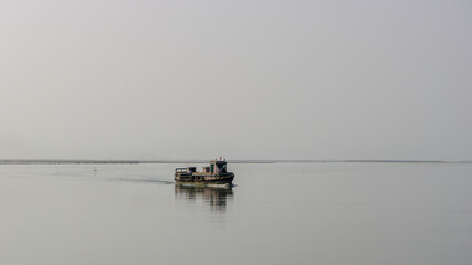 Wall Mural - Minimalist landscape view of small wooden ferry boat crossing the mighty Brahmaputra river in Assam, India
