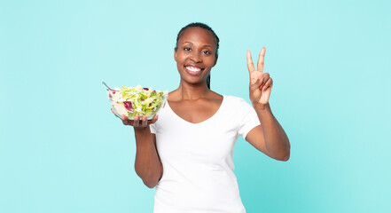 smiling and looking friendly, showing number two and holding a salad