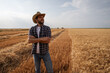 © djoronimo - Farmer is standing in front of his wheat field while harvesting is taking place.