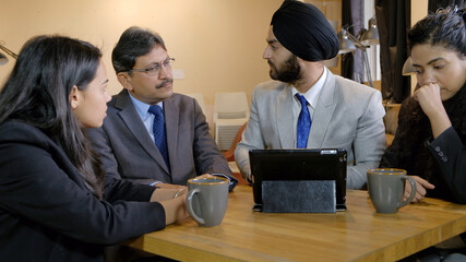 Poster - Team of South Asians from India working together with a tablet and coffee mugs on the table