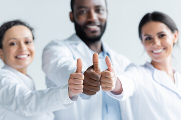 Wall Mural - Interracial doctors on blurred background showing thumbs up