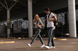 © Look! - Blonde curly woman in denim pants and plaid shirt talks with brunette man in jeans and white tee. Couple of travelers walks with backpacks near airport.