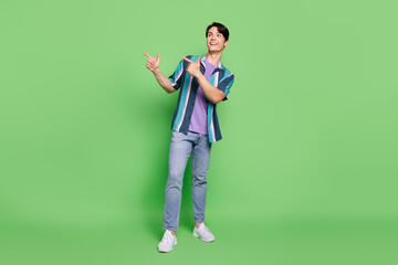 Full length photo of funky brunet young guy point look empty space wear shirt jeans isolated on green color background