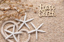Beach Or Tropical Theme Holiday Greeting With Glittery Balls On Twigs, White Starfish, Nautical Rope, And Peace On Earth On Beach Sand All In Natural Tones