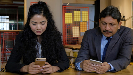 Poster - Young Indian worker and a middle-aged man on their smartphones in office