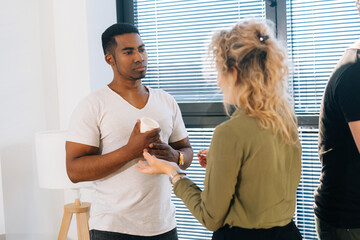 Middle shot portrait of serious African American male having conversation with young woman colleague during break. Two multiethnic coworkers enjoy pleasant communication, discuss project by window.