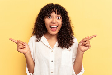 Poster - Young mixed race woman isolated on yellow background pointing to different copy spaces, choosing one of them, showing with finger.