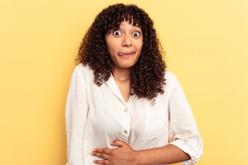 Wall Mural - Young mixed race woman isolated on yellow background touches tummy, smiles gently, eating and satisfaction concept.