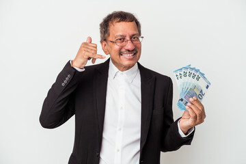 Middle aged indian business man holding bills isolated on white background showing a mobile phone call gesture with fingers.