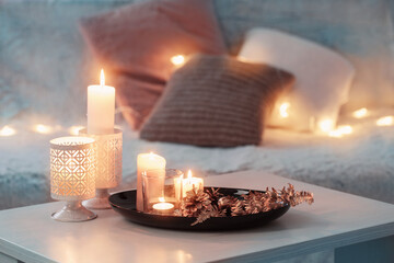 Christmas decoration   with burning candles on  white table against the background of  sofa with plaids and pillows. Cozy home and holiday concept