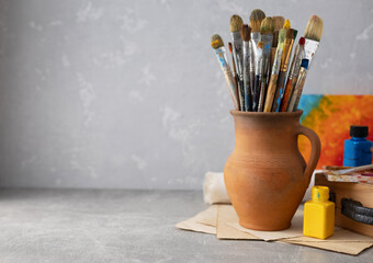 Poster - Paint brush in clay jug and art painter tool on table background texture. Paintbrush for painting