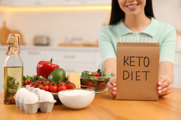 Canvas Print - Happy woman holding notebook with words Keto Diet near different products in kitchen, closeup