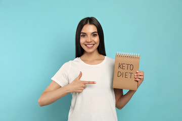 Poster - Happy woman holding notebook with words Keto Diet on turquoise background