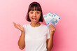 © Asier - Young mixed race woman holding bills isolated on pink background surprised and shocked.