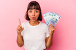 © Asier - Young mixed race woman holding bills isolated on pink background having some great idea, concept of creativity.