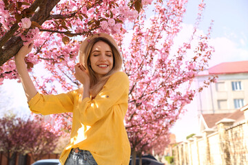 Sticker - Happy stylish young woman near blossoming sakura tree outdoors. Spring look