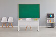 © Studio Romantic - Interior of a modern light empty school classroom with a clean green blackboard, teacher's desk, chairs, shelf, books and earth globe. Education and back to school concept