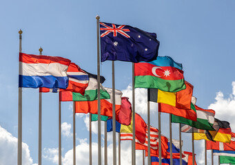 Many flags of various states - as a symbol of world cooperation. Flags of the countries of the world on flagpoles fluttering in the wind against the background of a cloudy sky