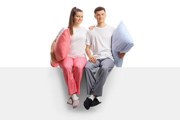Wall Mural - Full length portrait of a young couple in pajamas posing in embrace seated on a panel