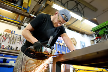 Canvas Print - Metalwork craftsman cutting metal with grinder tools. Worker man in protection gloves and glasses working in the workshop. Small local business.